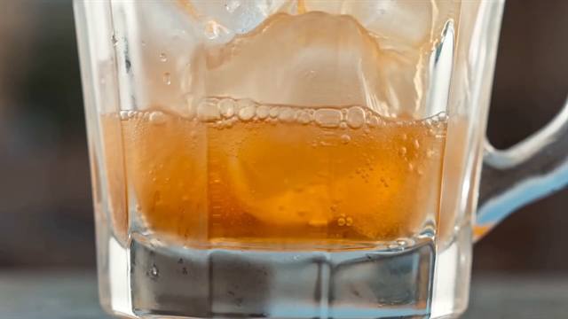 Macro shot of an amber soft drink over ice in a heavy glass, condensation running down the outside.