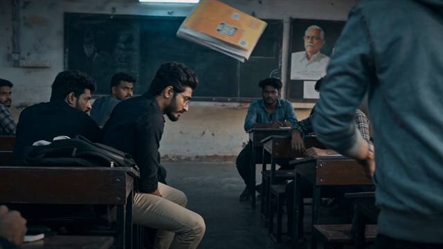 A textbook suspended in mid-air in a dim classroom while a figure crosses the foreground and the lead sits at a desk.